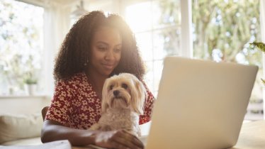 person in front of laptop with dog sitting in lap